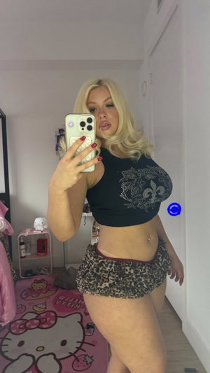 Blonde curvy woman in black crop top and leopard shorts in bedroom.