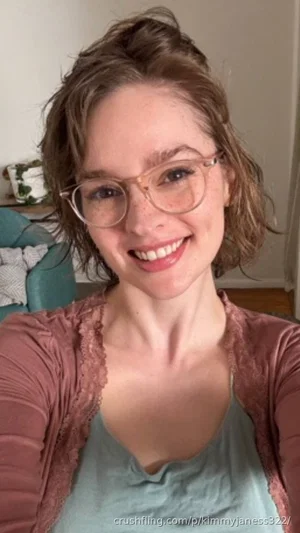 Woman with short brown hair and glasses, wearing a green top and pink cardigan, smiling in a casual