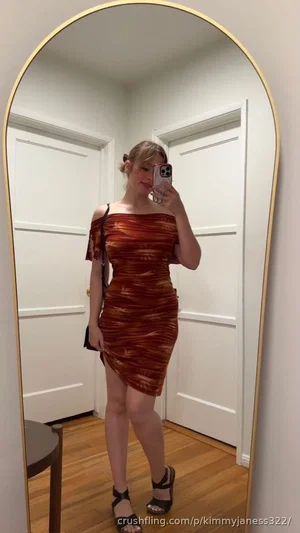 Woman in a red and brown striped off-shoulder dress, taking a mirror selfie indoors.