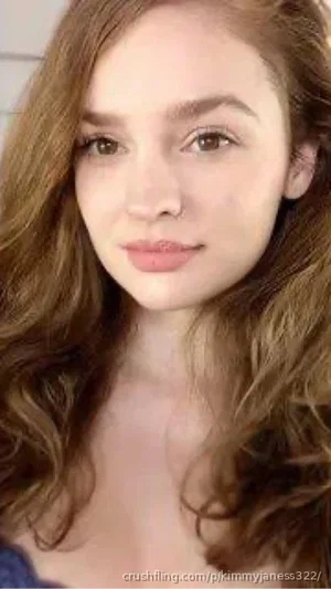 Woman with wavy brown hair, wearing a dark top, looking at camera indoors.