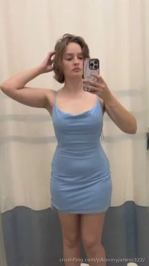 Woman in light blue dress taking mirror selfie, indoor setting.