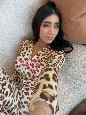 Woman in leopard print outfit lying on couch, dark hair, makeup, casual pose.