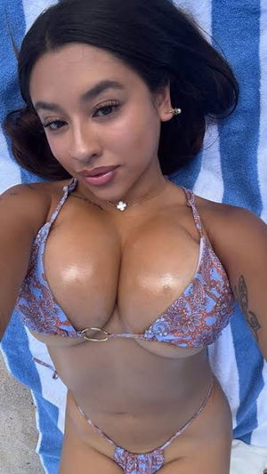 Woman in floral bikini lying on blue striped towel, dark hair, tattoo on arm.