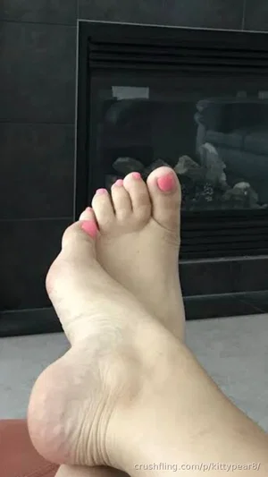 Bare feet with pink toenail polish in front of a fireplace.