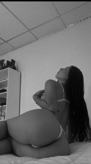 Woman in white lingerie posing on bed, back view, long dark hair, indoor setting.