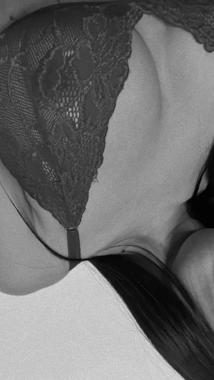 Woman in black lace lingerie, close-up of chest and shoulder, indoor setting.