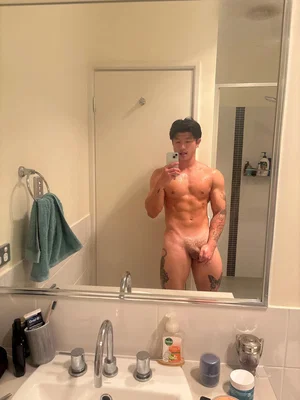 Muscular man taking mirror selfie in bathroom.