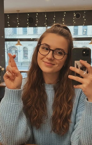 Woman with glasses and long brown hair in blue sweater taking selfie.