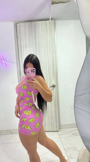 Woman in pink avocado-print bodysuit taking mirror selfie in bedroom.