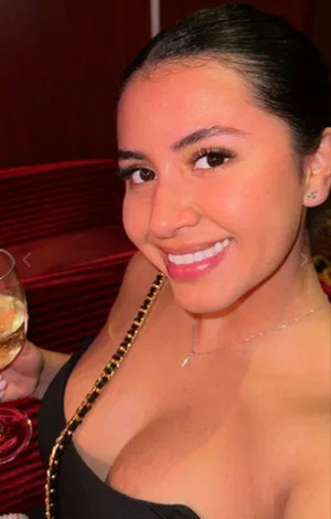 Woman with dark hair in black top holding wine glass, smiling in red booth.