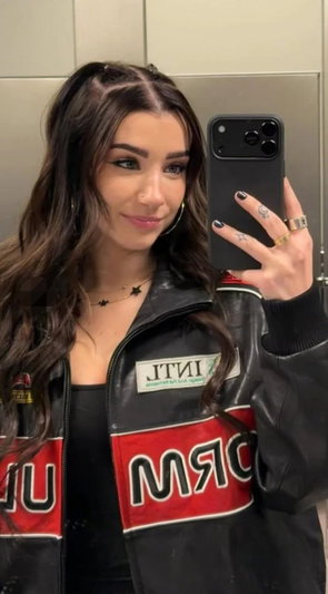 Woman with long dark hair taking mirror selfie in leather jacket.