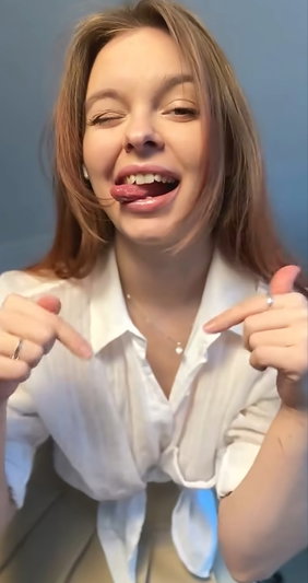 Woman with light brown hair in white shirt making playful face indoors.