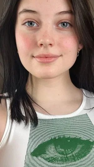 Woman with dark hair and green eyes wearing a white tank top with a green eye graphic.