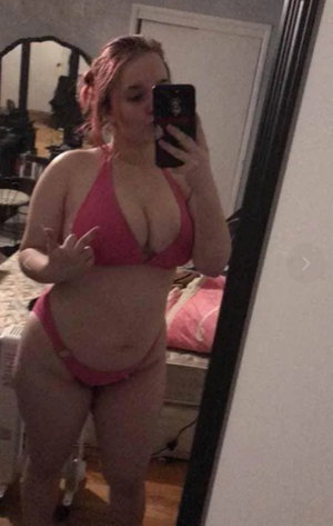 Woman in pink bikini taking mirror selfie in bedroom.