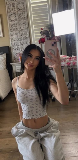 Dark-haired woman in crop top and sweatpants taking mirror selfie.