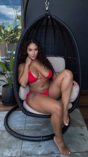 Woman in red bikini sitting in hanging chair outdoors, curly hair, bare feet.