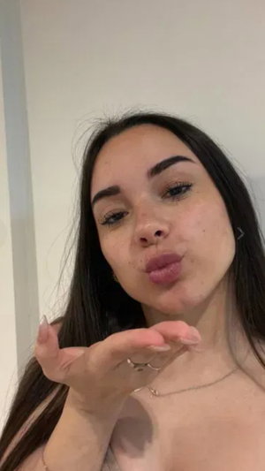 Dark-haired woman with freckles blowing a kiss indoors.
