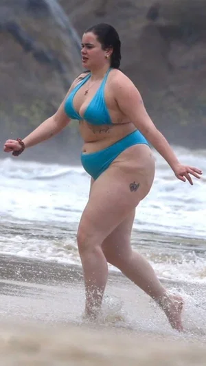 Woman in blue bikini walking in shallow ocean water at beach.