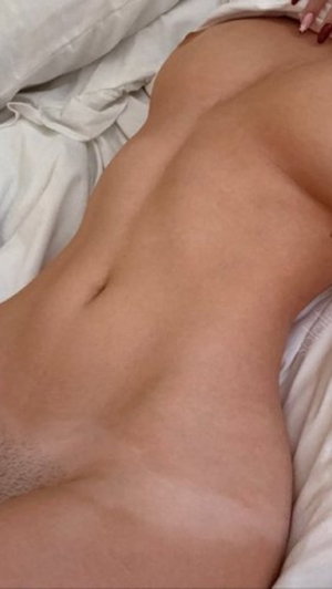 Woman with toned midsection lying on white sheets, partial back view.