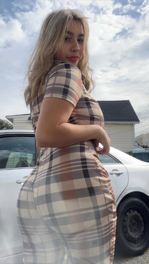 Curvy blonde in plaid bodysuit posing outdoors by car.