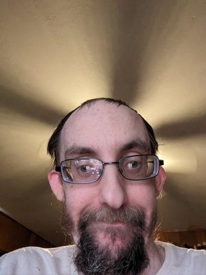 Man with glasses and beard wearing white shirt indoors.