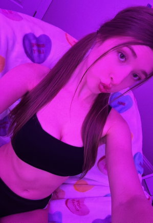 Woman with long brown hair in black crop top on bed.