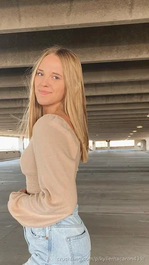 Blonde woman in beige top and jeans posing under concrete overpass.