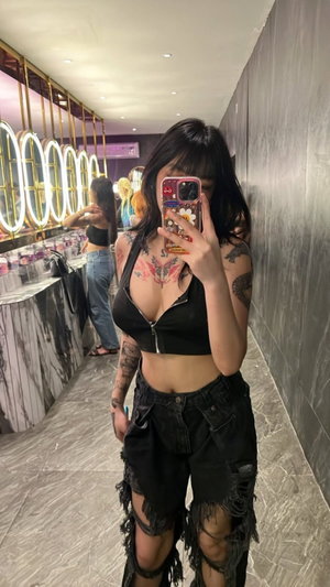 Asian woman with tattoos taking mirror selfie in black top and shorts.