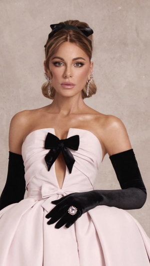 Woman in pink strapless dress with black bow and long gloves.