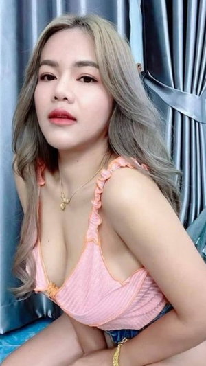 Asian woman with long hair in pink top and shorts indoors.