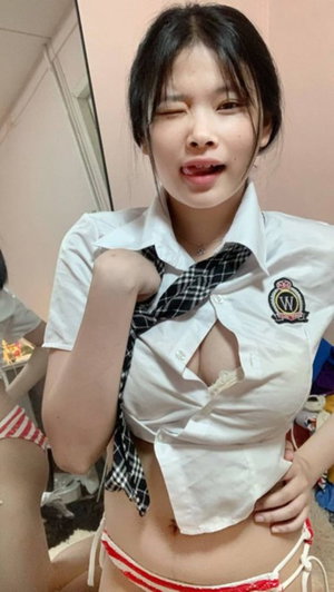 Asian woman in open white shirt and striped bottoms posing indoors.