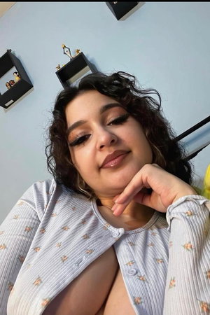Woman with curly hair in floral top taking selfie indoors.