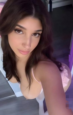 Dark-haired woman in pink lingerie taking a bedroom selfie.