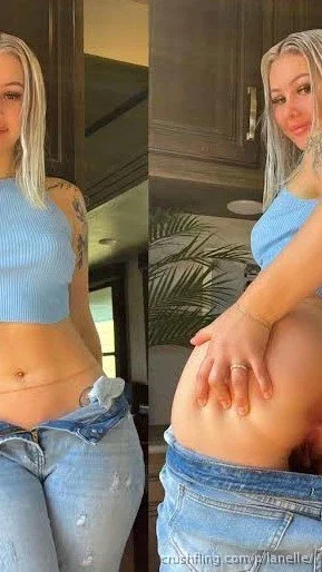 Woman with blonde hair in blue crop top and jeans, posing indoors with hand on hip.