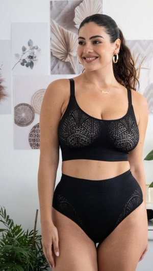 Woman in black lace lingerie standing indoors, smiling at camera.