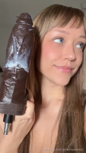 Woman with long hair holding a chocolate-covered object, indoors, smiling.