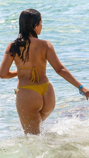 Woman in yellow bikini walking in shallow ocean water, back view.