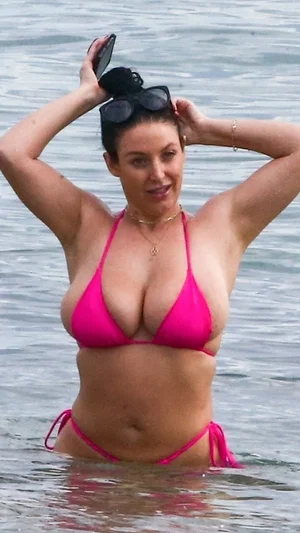 Woman in pink bikini standing in water, holding sunglasses on head.
