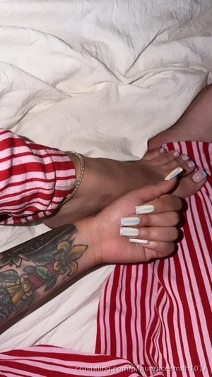 Person with tattooed arm and striped pajamas resting hands and feet on bed.