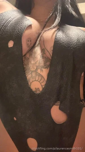 Woman with dark hair and chest tattoo wearing black cut-out top, indoor setting.