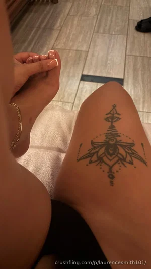 Woman with tattoo on thigh, wearing black bottoms, sitting on towel indoors.