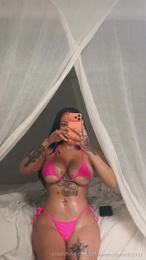Woman in pink bikini with tattoos takes mirror selfie in bedroom.