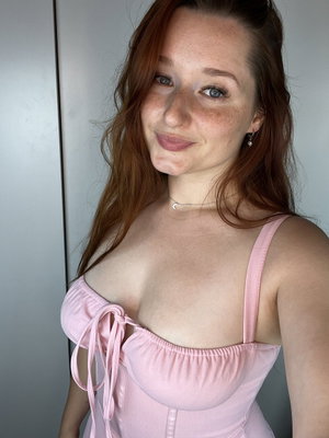 Woman with red hair in pink top, smiling indoors.