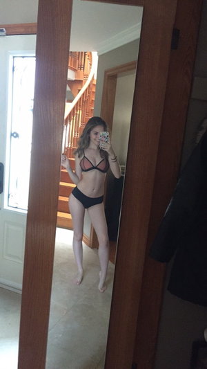 Woman in black lingerie taking mirror selfie in home hallway.
