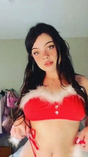 Woman with black hair in red fur-trimmed lingerie in bedroom.