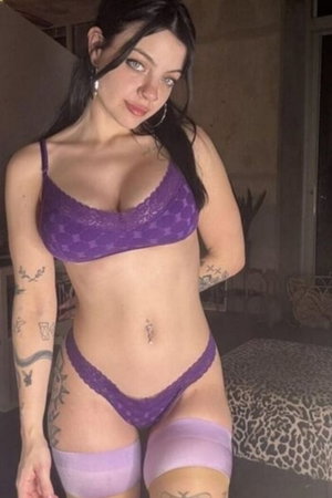 Curvy woman with dark hair in purple lace lingerie indoors.