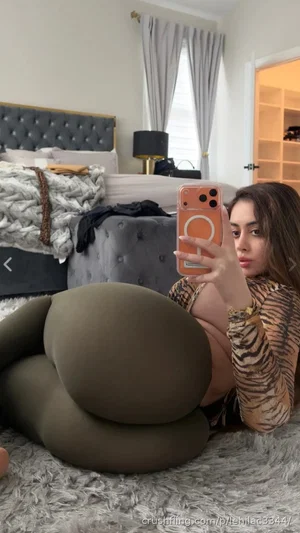 Woman in tiger-print top and olive green leggings takes mirror selfie in bedroom.