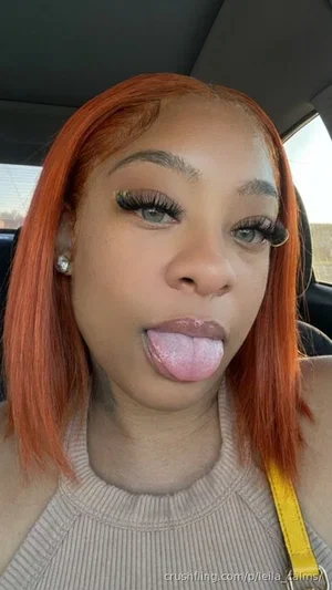 Woman with orange hair and green eyes sticking tongue out, wearing beige top, inside car.