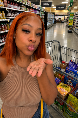 Woman with red hair in a tank top posing in a grocery store aisle with a shopping cart.