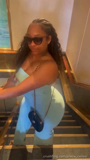 Woman in light blue dress with curly hair, sunglasses, and chain purse on staircase.